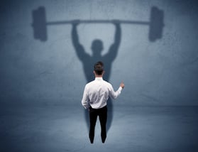 A confident young elegant salesman with briefcase facing a wall, looking at his strong, weight lifting shadow concept