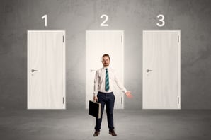 Businessman in grey room with three numbered white  door behind his back