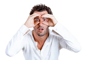 Closeup portrait of young, curious guy, funny man, looking through his fingers like binoculars, searching for something, surprised shocked by what is waiting him in future isolated on white background