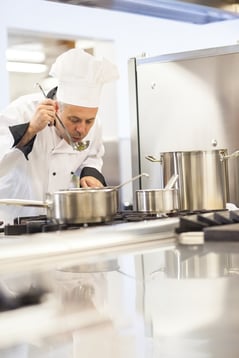 Concentrating head chef tasting food from ladle in professional kitchen