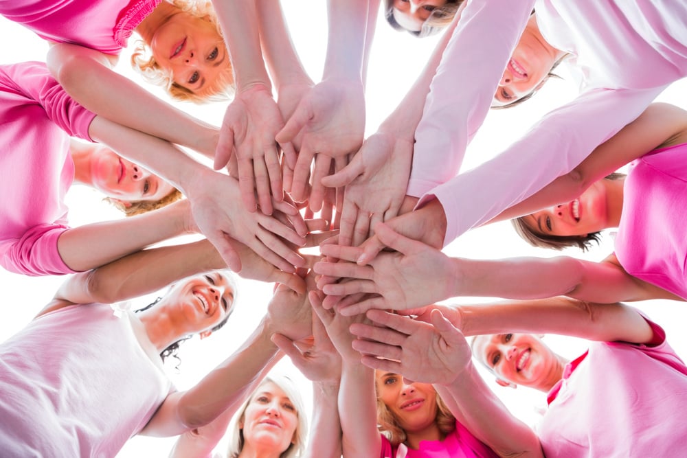 Diverse women smiling in circle wearing pink for breast cancer on white background