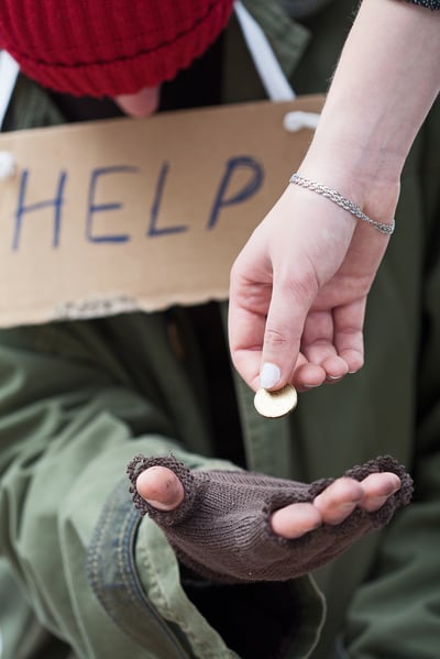 Rich woman giving a coin to homeless man in need